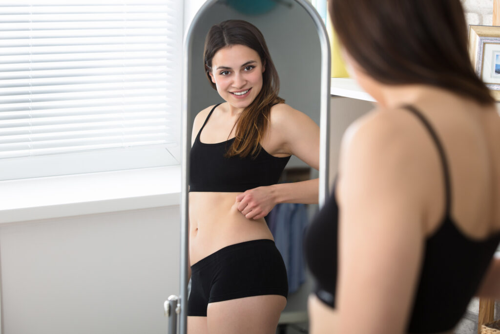 Woman checking her figure in the mirror, considering liposuction options.